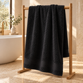 black Sofia 90x160 cm cotton bath sheet – styled on an oak towel stand in a spa bathroom